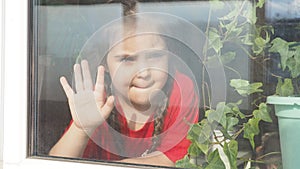 Beautiful little girl smiling and watching out the window. A child looks out the window. Portrait of cheerful kid. self