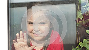 Beautiful little girl smiling and watching out the window. A child looks out the window. Portrait of cheerful kid. self