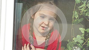 Beautiful little girl smiling and watching out the window. A child looks out the window. Portrait of cheerful kid. self