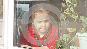 Beautiful little girl smiling and watching out the window. A child looks out the window. Portrait of cheerful kid. self