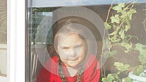 Beautiful little girl smiling and watching out the window. A child looks out the window. Portrait of cheerful kid. self