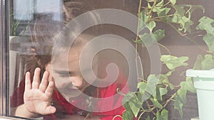 Beautiful little girl smiling and watching out the window. A child looks out the window. Portrait of cheerful kid. self