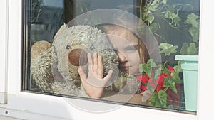 Beautiful little girl smiling and watching out the window. A child looks out the window. Portrait of cheerful kid. self