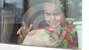 Beautiful little girl smiling and watching out the window. A child looks out the window. Portrait of cheerful kid. self