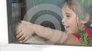 Beautiful little girl smiling and watching out the window. A child looks out the window. Portrait of cheerful kid. self