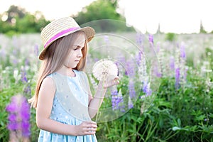 Beautiful little girl standing on a flowering field in green grass and holds a dandelion. Enjoy the nature. Healthy smiling girl o