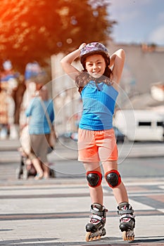 Beautiful little girl stands in roller skates at a city park in the sunshiny summer day.