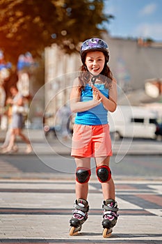 Beautiful little girl stands in roller skates at a city park in the sunshiny summer day. photo