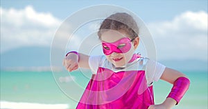 Beautiful little girl in the superhero costume, dressed in a pink cloak and the mask of the hero. Plays on the