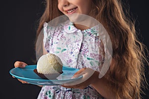 Beautiful little girl surprised from a tasty big chocolate coconut candy as a ball. Kid ready to eat cake
