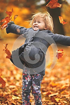 Beautiful little girl throwing yellow autumn leaves in the air in the park; autumn background