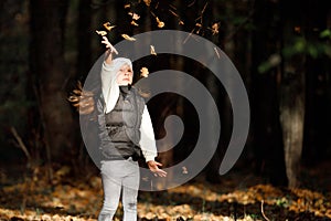 Beautiful little girl wearing playing with dry leaves throwing them into the air