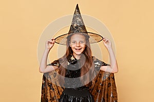 Beautiful little girl wearing witch costume and carnival cone hat isolated over beige background kid sorcerer lookingat camera photo