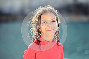 Beautiful little girl with wet hair smiling and looking at camera at beach during sunset, Outdoor portrait of happy child