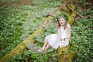 Beautiful  little girl in a white dress plaing with white rabbit in the spring wood