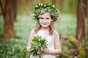 Beautiful  little girl in a white dress  in the spring wood. Portrait of the pretty little girl with a wreath from spring flowers