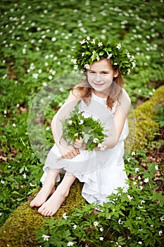 Beautiful  little girl in a white dress walks in the spring wood. Portrait of the pretty little girl with a wreath from spring