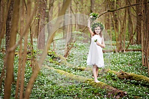 Beautiful  little girl in a white dress walks in the spring wood. A portrait of the pretty little girl with a wreath from spring
