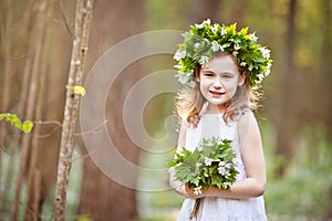 Beautiful  little girl in a white dress walks in the spring wood. A portrait of the pretty little girl with a wreath from spring