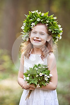 Beautiful  little girl in a white dress walks in the spring wood. Portrait of the pretty little girl with a wreath from spring