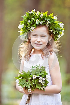 Beautiful  little girl in a white dress walks in the spring wood. Portrait of the pretty little girl with a wreath from spring