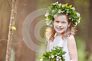 Beautiful  little girl in a white dress walks in the spring wood. Portrait of the pretty little girl with a wreath from spring