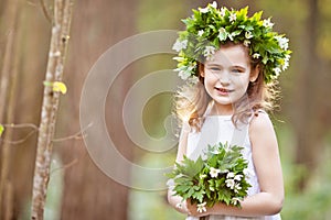 Beautiful  little girl in a white dress walks in the spring wood. Portrait of the pretty little girl with a wreath from spring