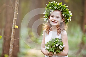 Beautiful  little girl in a white dress walks in the spring wood. Portrait of the pretty little girl with a wreath from spring