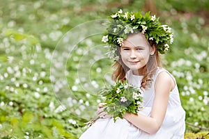 Beautiful  little girl in a white dress walks in the spring wood. Portrait of the pretty little girl with a wreath from spring