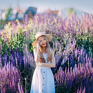 Beautiful little girl in white hat and dress smiling in the park