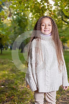 Beautiful little girl in white sweater posing in autumn Park near the tree