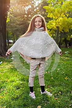 Beautiful little girl in white sweater posing in autumn Park near the tree