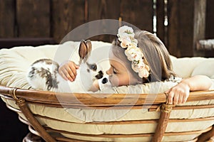 Beautiful little girl in a wreath of flowers kisses a cute fluffy white Easter bunny