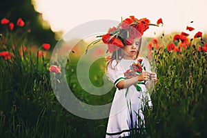 Beautiful little girl with a wreath of poppies on head. cute child in wild poppies field