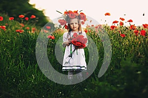 Beautiful little girl with a wreath of poppies in a white dress and a bouquet of wildflowers. cute child in poppy field