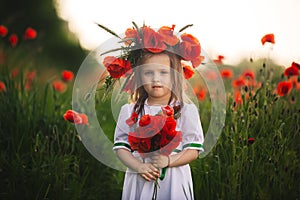 Beautiful little girl with a wreath of poppies in a white dress and a bouquet of wildflowers. cute child in poppy field