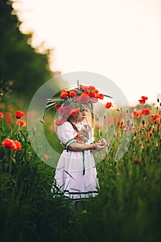 Beautiful little girl with a wreath of poppies in a white dress and collects a bouquet of wildflowers. cute child in poppy field