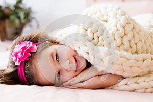 Beautiful little girle laying under the white knitted blanked, s