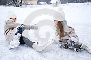 Beautiful little girls, sisters learn to skate on ice skating rink in park. Fall and have fun. Stylish looks, warm woolen coats, photo