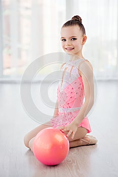 Beautiful little gymnast girl in pink sportswear dress, performing art gymnastics element with ball in fitness class