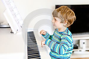 Beautiful little kid boy playing piano in living room or music school