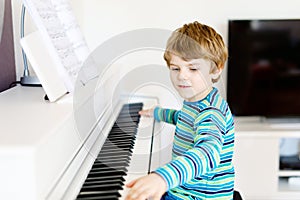 Beautiful little kid boy playing piano in living room or music school