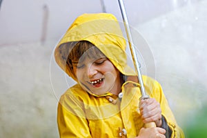 Beautiful little kid boy on way to school walking during sleet, heavy rain and snow with an umbrella on cold day. Happy