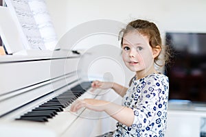 Beautiful little kid girl playing piano in living room or music school