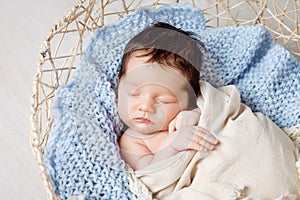 Beautiful little newborn baby 2 weeks sleeping in a basket with knitted plaid. Portrait of pretty  newborn baby