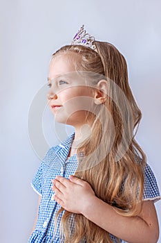 Beautiful little princess girl in silver crown holding magic wand smiling. Young lady with long wavy hair in blue dress