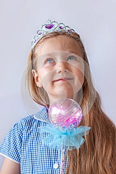 Beautiful little princess girl in silver crown holding magic wand smiling. Young lady with long wavy hair in blue dress