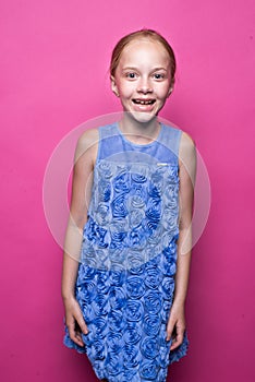 Beautiful little redhead girl in blue dress posing like model on pink background.