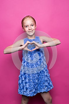 Beautiful little redhead girl in blue dress posing like model on pink background.