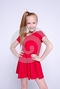 Beautiful little redhead girl in red dress posing like model on white background.